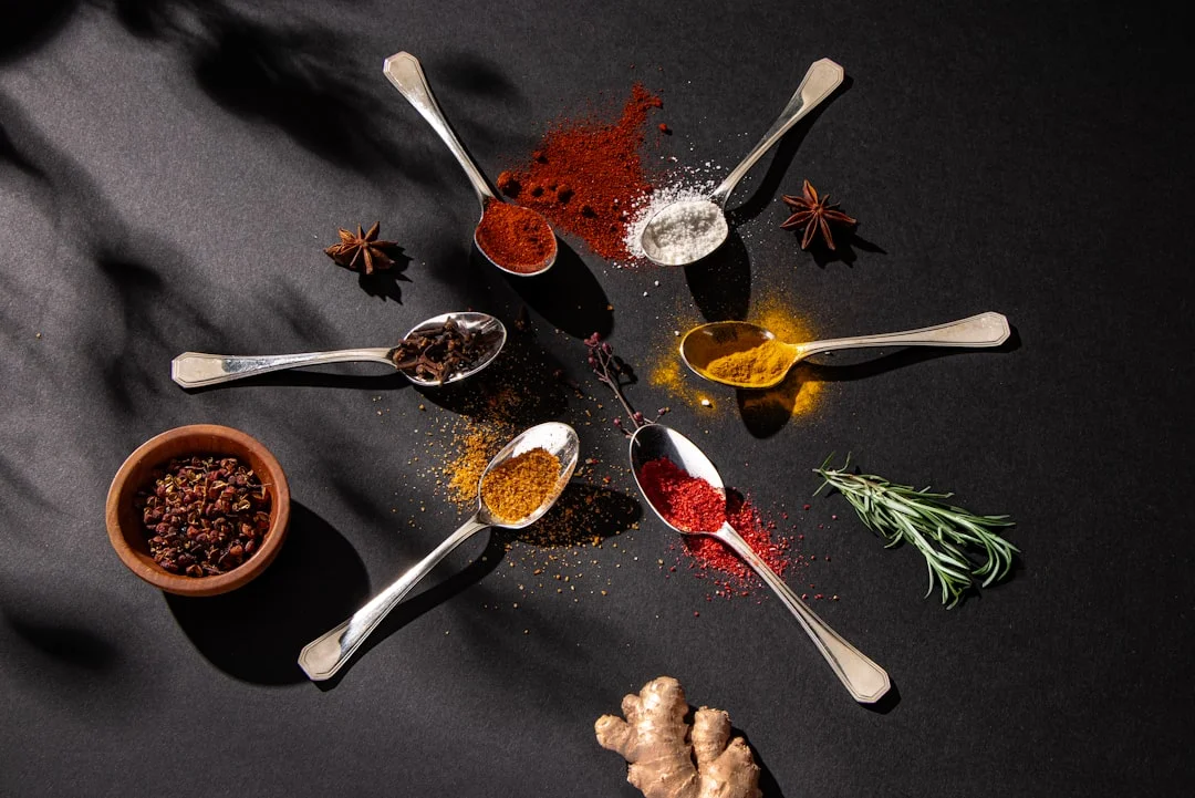 Close-up of three amber glass bottles of pure vanilla extract and vanilla bean paste arranged on a marble pastry counter beside split vanilla pods and a mixing bowl dusted with flour